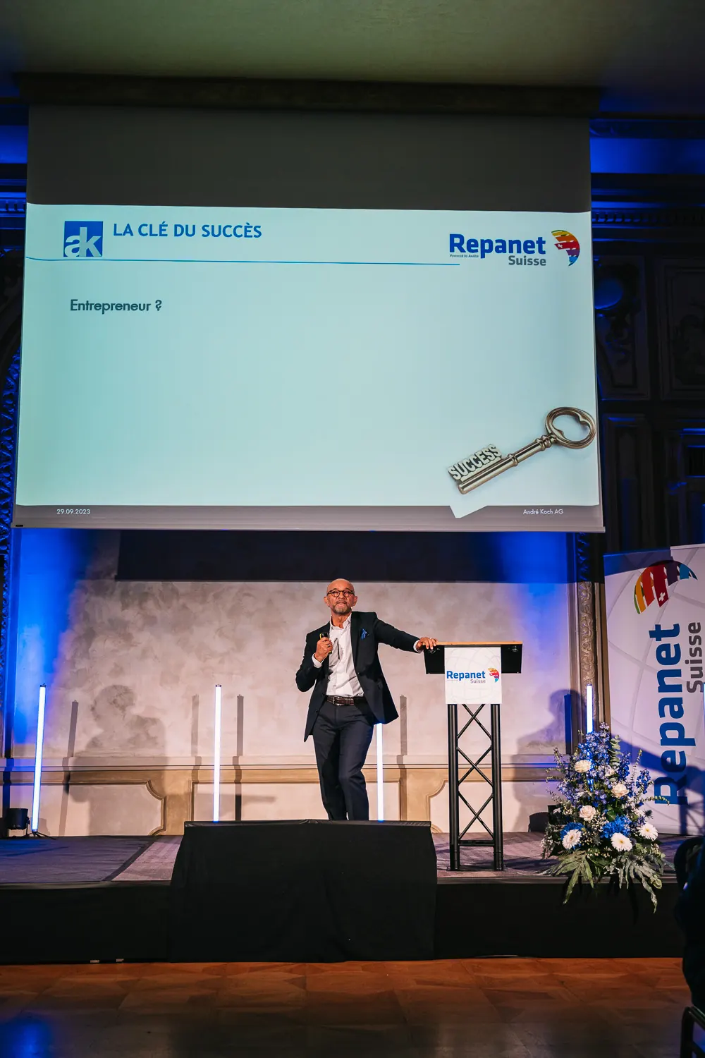 Enzo Santarsiero spricht auf der Bühne eines festlichen Saals, auf der Leinwand ein Schlüssel