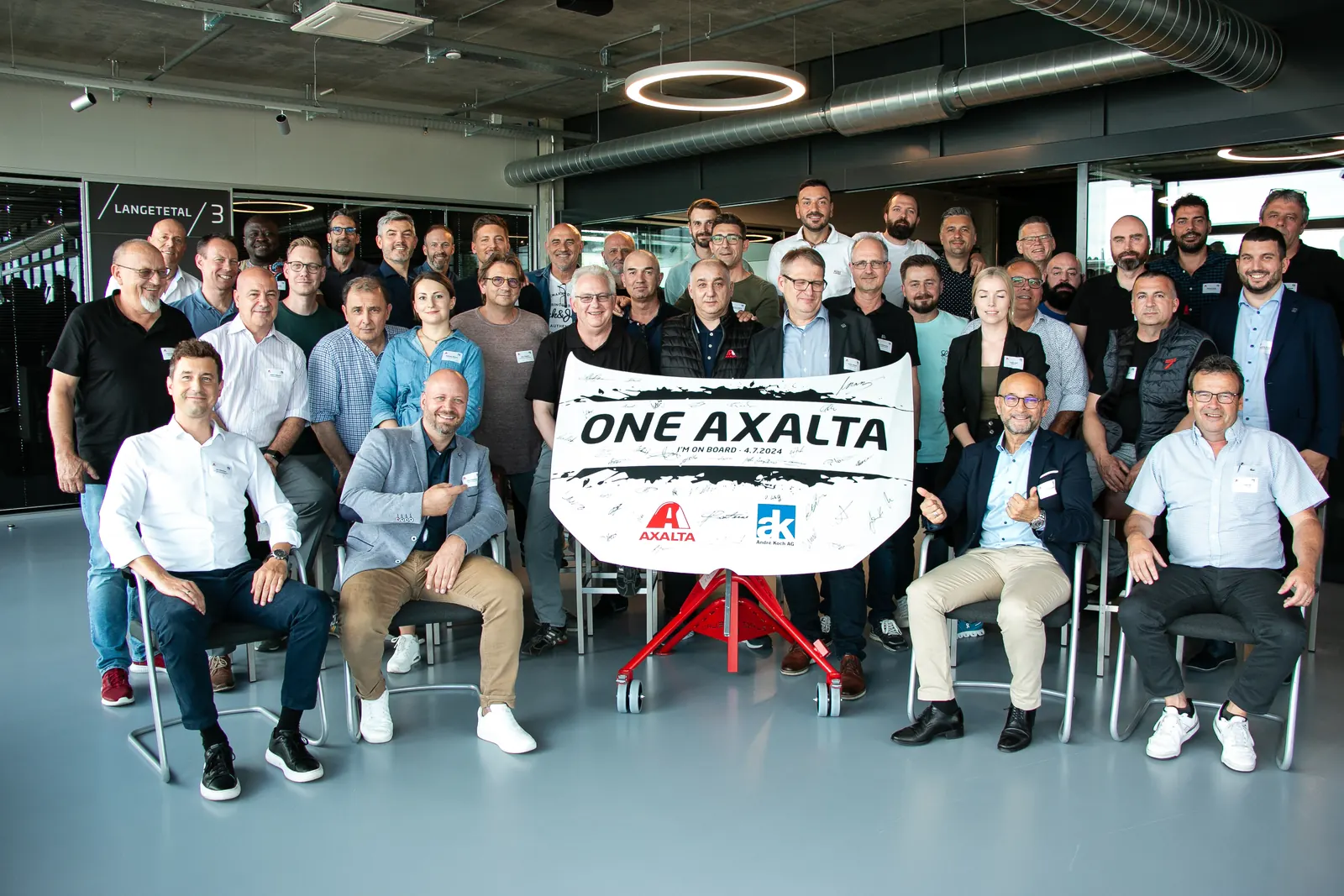 Gruppenbild von rund vierzig Personen um ein Transparent „One Axalta“